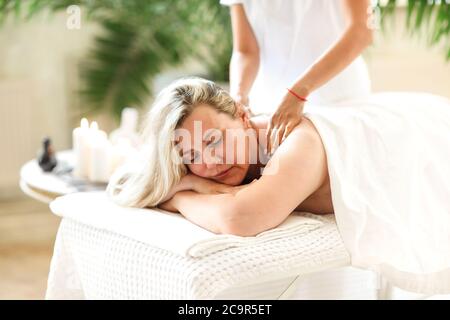 Side view of ethnic female therapist massaging face of middle age woman lying on massage table in spa salon Stock Photo