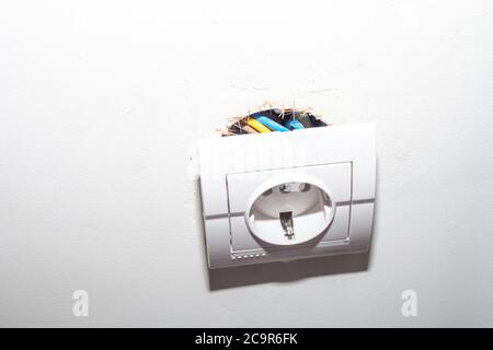 Broken electric socket torn from white wall. Fixing loose electrical outlet box Stock Photo