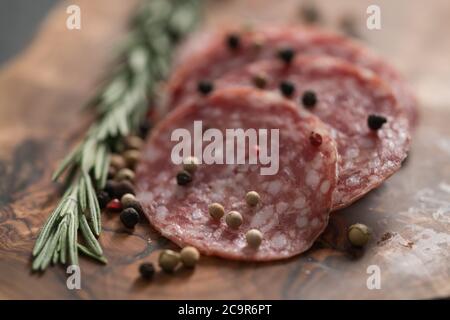 Sliced salame milano sausage on olive wood board with rosemary and pepper Stock Photo