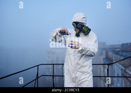 Researcher of the laboratory is conducting the study with blue reagent in glass flask, working on roof of high building, concept of global radiation Stock Photo