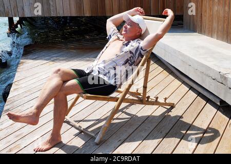 smiling man resting on a sun lounger on the patio near the sea Stock Photo