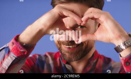 Portrait of smiling young man keeps hands over his eye in heart shape , expresses sympathy. Close up. High quality photo Stock Photo