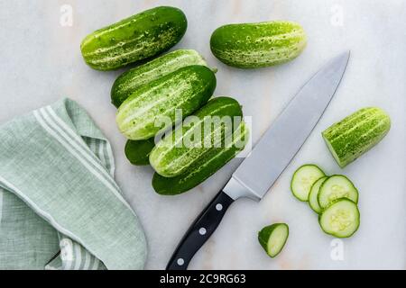 Photograph of freshly picked organic pickling cucumbers, being prepared for slicing with a chef's knife and dishtowel on kitchen counter Stock Photo