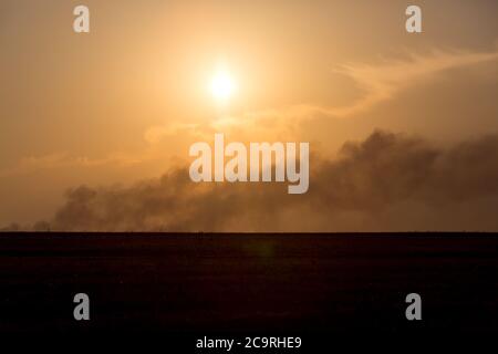 On the horizon in are far a smoke column from the fire at sunset. Stock Photo