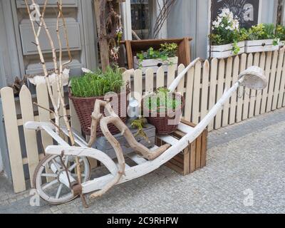 Czech Republic, Prague, Karlin, May 11, 2018: white wooden wheelbarrow with flowers in wicker basket, florist shop window, entrance decorated with dry Stock Photo