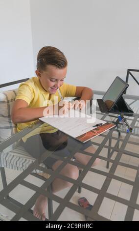 Young boy doing homework at home on dining room table concentrating and thinking while school is on a break. Stock Photo