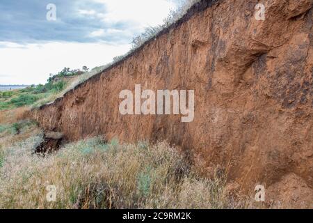 layers of earth with cracks due to landslides of the soil ecological disaster in outdoor clay wall under cloudy sky. Stock Photo