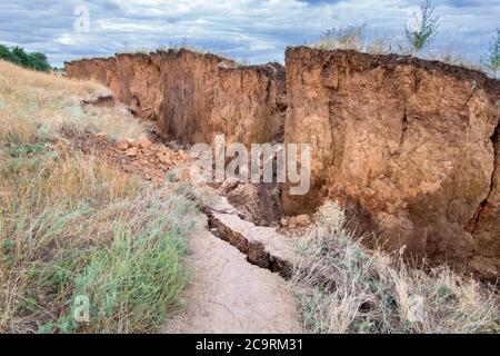 layers of earth with cracks on trail path due to landslides of the soil ecological disaster in outdoor clay wall under cloudy sky. Stock Photo