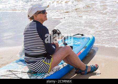 Poole, Dorset UK. 2nd August 2020. Dog training sessions on the beach with dogs learning to paddleboard and increase their balance and confidence in the sea on a lovely warm sunny day. Cavapoochon cross between three breeds – a Cavalier King Charles spaniel, a poodle and a bichon frise, also known as 'the dog that never grows old' Credit: Carolyn Jenkins/Alamy Live News Stock Photo