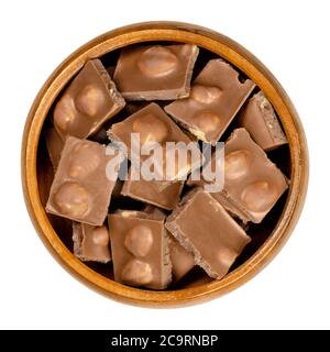 Hazelnut milk chocolate, bars broken into pieces, in wooden bowl. Small segments of candy bar. Milk chocolate with whole roasted hazelnuts. Stock Photo