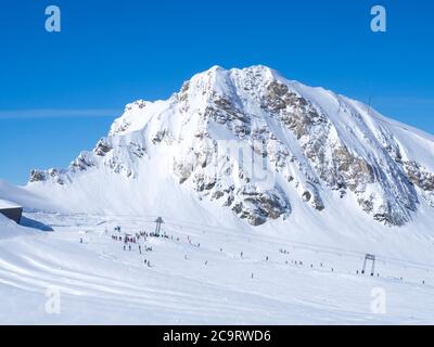 Winter mountains landscape with colorful dressed skiers on white snow slopes. view from the top of Kitzsteinhorn mountain, blue sky. Kaprun ski resort Stock Photo