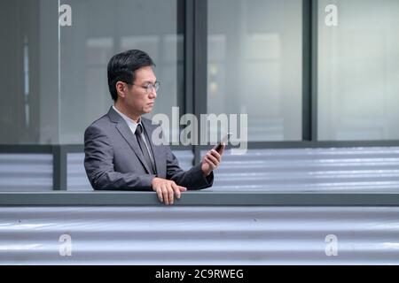 Chinese businessman in business suit and tie reading on his cellphone. Copy space. Stock Photo