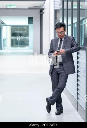 Chinese businessman in suit standing in style, using his cellphone. Stock Photo