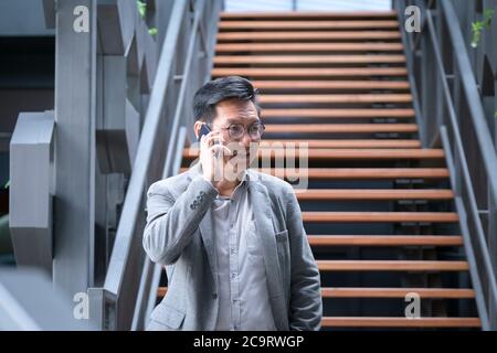 Chinese businessman standing at the bottom of the staircase talking on his cellphone Stock Photo