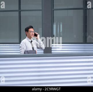 Chinese businessman standing, smiling and talking on his cellphone Stock Photo