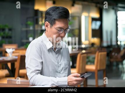 Chinese businessman wearing a jacket, smiling and looking at the cellphone in his hand. Stock Photo