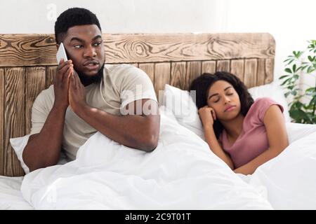 Black guy talking with lover on cellphone in bed Stock Photo