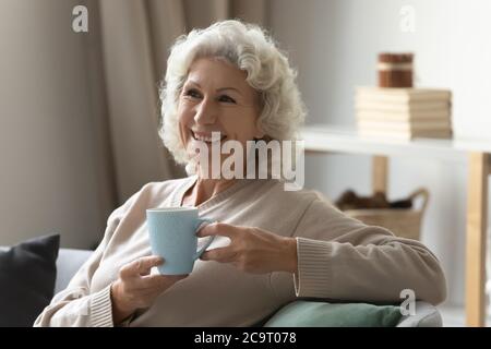 70s woman lean on couch drinking tea laughs feels carefree Stock Photo