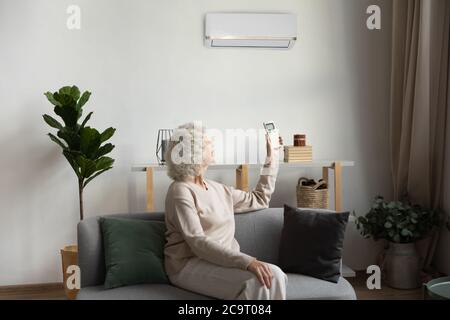 Elderly woman holding airconditioner remote control set comfortable temperature indoors Stock Photo