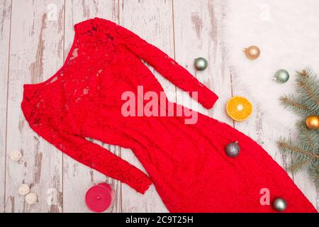 Red elegant lace dress on a wooden background, fir branch with ornaments and citrus. Fashion concept. Close-up Stock Photo