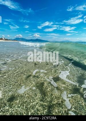 Calm sea wave on an empty beach with a long promenade, mountain views and beautiful blue skies and white clouds. Summer scene, seascape