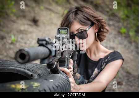 Beautiful and attractive woman soldier shooting with rifle machine gun from behind and around cover or barricade. Female  army military combat trainin Stock Photo