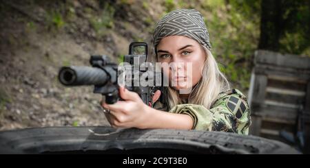 Beautiful and attractive woman soldier shooting with rifle machine gun from behind and around cover or barricade. Female  army military combat trainin Stock Photo
