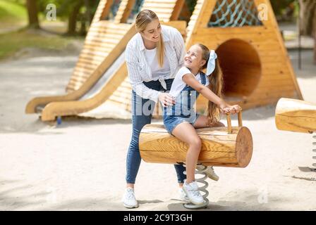 Mother Pushing Daughter On Swing Having Fun On Playground Outside Stock Photo