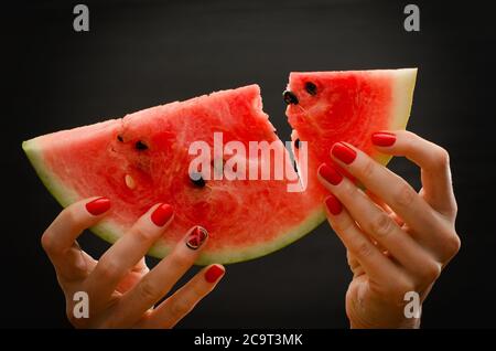 Broken big slice of ripe watermelon in female hands on a black background, close-up Stock Photo