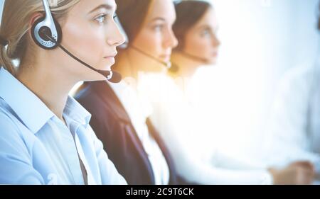 Cheerful smiling business woman with headphones consulting clients. Group of diverse phone operators at work in sunny office.Call center and business Stock Photo