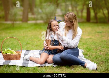 Young Mother Touching Daughter's Nose Having Picnic Outside In Park Stock Photo
