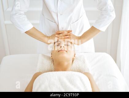 Beautiful blonde woman enjoying facial massage with closed eyes. Relaxing treatment in medicine and spa center concepts Stock Photo