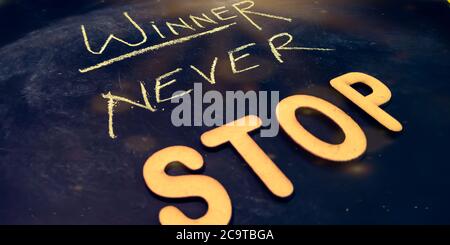 Winner never stop text presented for active business education concept on chalkboard abstract background. Stock Photo