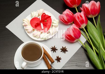 Gingerbread heart shaped pink tulips and a mug of coffee. Black table. top view Stock Photo