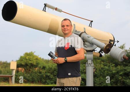 17 July 2020, Saxony-Anhalt, Parey: Thomas Becker, hobby astronomer, is standing in front of his telescope in Parey /Havelaue. As a nature park employee, Becker is in charge of the 'Sternenpark' project and brings it closer to guests, for example during nightly starwalks. For the tourism industry in Havelland and Altmark, this offers the chance to attract new groups of visitors. Many accommodation providers have already adapted to the special clientele. Telescopes and hire telescopes are also part of the offer, as is the possibility of a late checkout after a nocturnal star trek. Photo: Peter Stock Photo