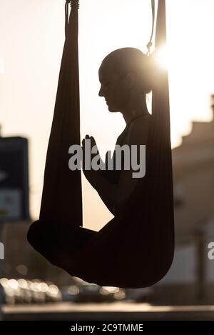 backlight young woman doing yoga on a red swing on wooden platform by the sea on a sunny day Stock Photo
