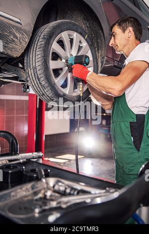 Mechanic in uniform is working in auto service with lifted vehicle Stock Photo