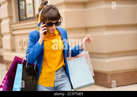 girl on a bright background with packages after shopping. Busy girl holds a lot of packages and a mobile phone on a bright background Stock Photo