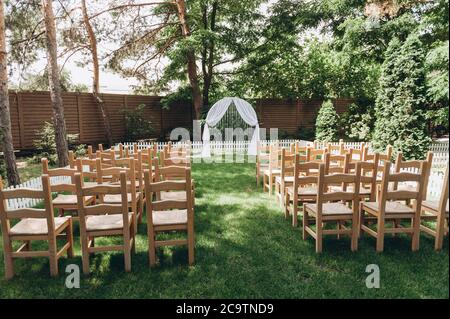wedding ceremony without people in the woods. The style of the Rustic. Wooden chairs and white wedding arch. Stock Photo