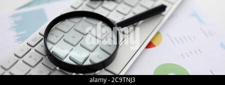 Black magnifying glass lies on white laptop keyboard closeup background. Stock Photo