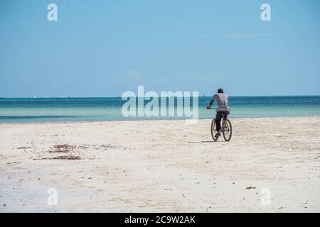 Man riding on a bike at the diani beach in Kenya. Beautiful view on ocean. Stock Photo