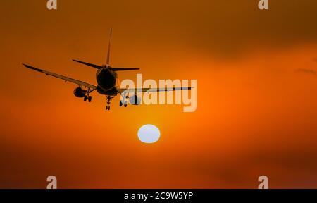 Silhouette of airplane during landing in front of amazing evening sky with sun, space for text Stock Photo