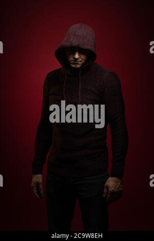 A man in a jumper with a hood and with a phone in his hands poses against a dark red background Stock Photo
