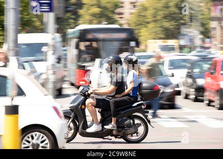 Belgrade, Serbia - July 21, 2020: Young couple riding a scooter vespa motorbike in busy city street traffic, on the crossroad with people and cars Stock Photo