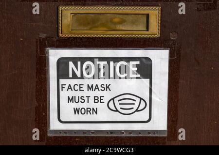 a notice on a front door of a business stating that face masks must be warn in accordance with government guidelines during the Covid-19 Stock Photo