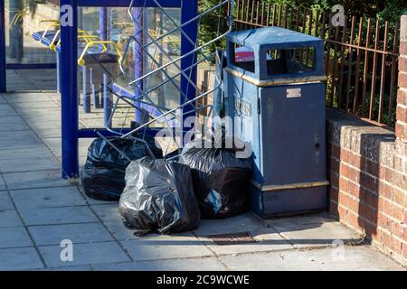 rubbish dumped or fly tipped in the street next to a litter bin Stock Photo