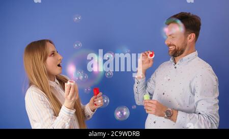 Young silly caucasian couple blowing bubbles and having fun. Isolated on blue background. High quality photo Stock Photo