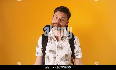 Disappointed face expression on young bearded traveler with backpack isolated on orange background. High quality photo Stock Photo