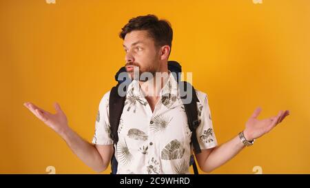 Disappointed face expression on young bearded traveler with backpack isolated on orange background. High quality photo Stock Photo