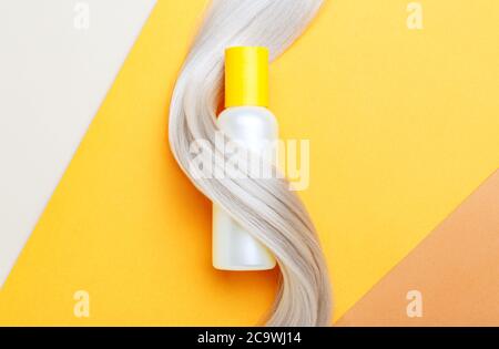 Shampoo bottle mockup strand in lock curl of blonde hair on orange color background. Yellow bottle shampoo. Flat lay copy space. Hair care cosmetics Stock Photo